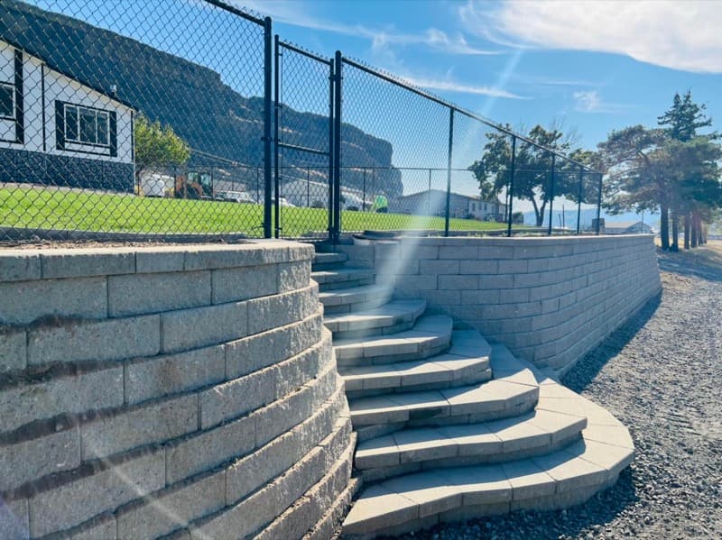 Curved block retaining wall with wide stairs and a chain-link fence
