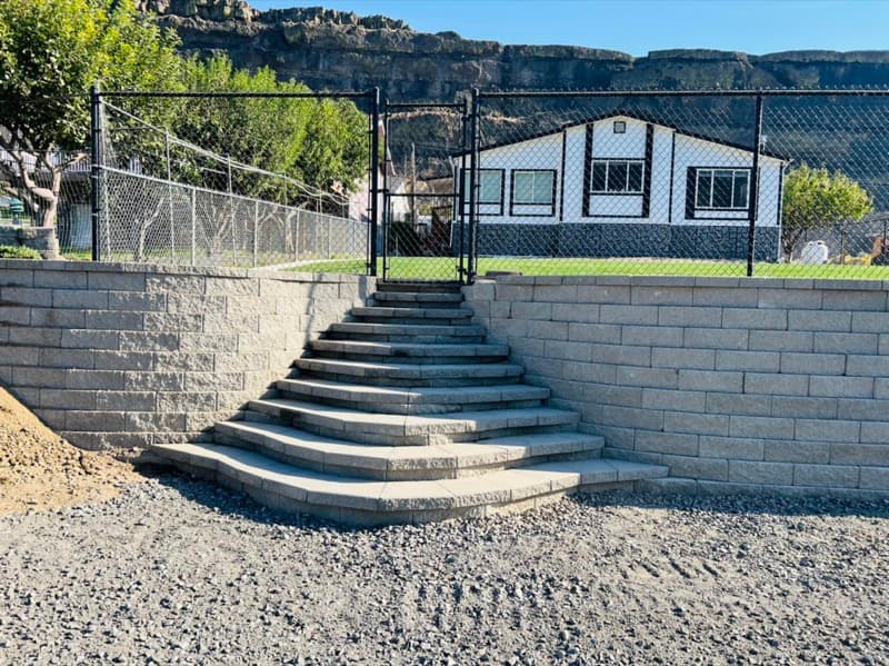 Block retaining wall with curved stairs and a chain-link fence