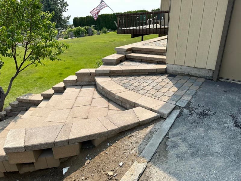 Curved paver steps leading up to a paver patio beside a lawn