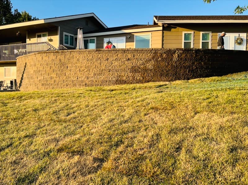Tall block retaining wall holding back a sloped yard