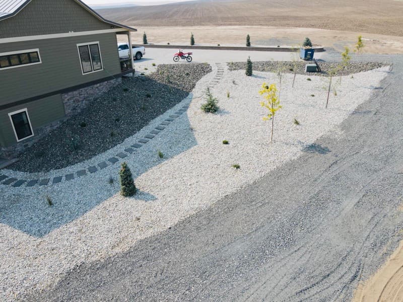 Decorative rock landscaping with young trees and paver edging around a new home