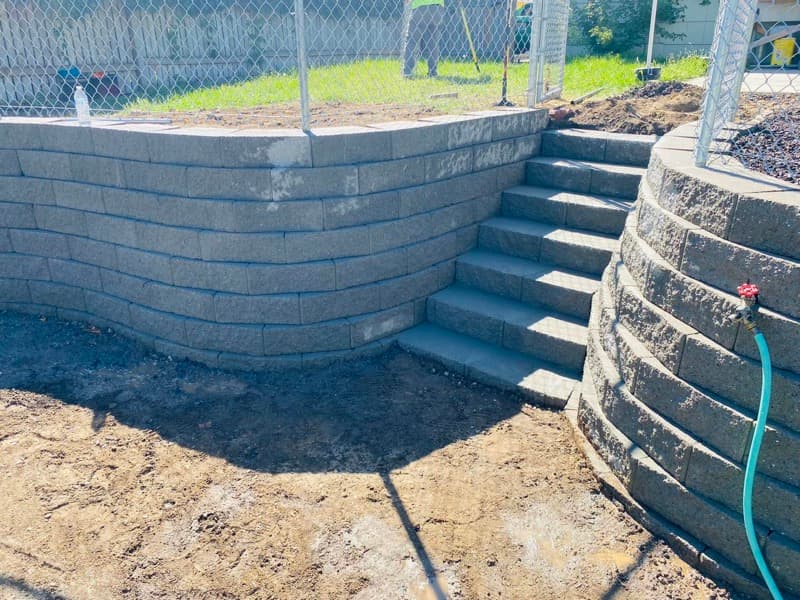 Curved block retaining wall with stairs and a chain-link fence