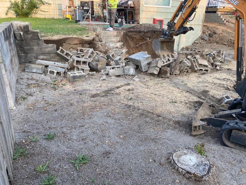 Failing block wall being demolished with an excavator