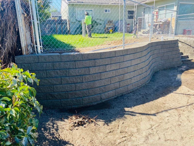 Curved block retaining wall beside a chain-link fence